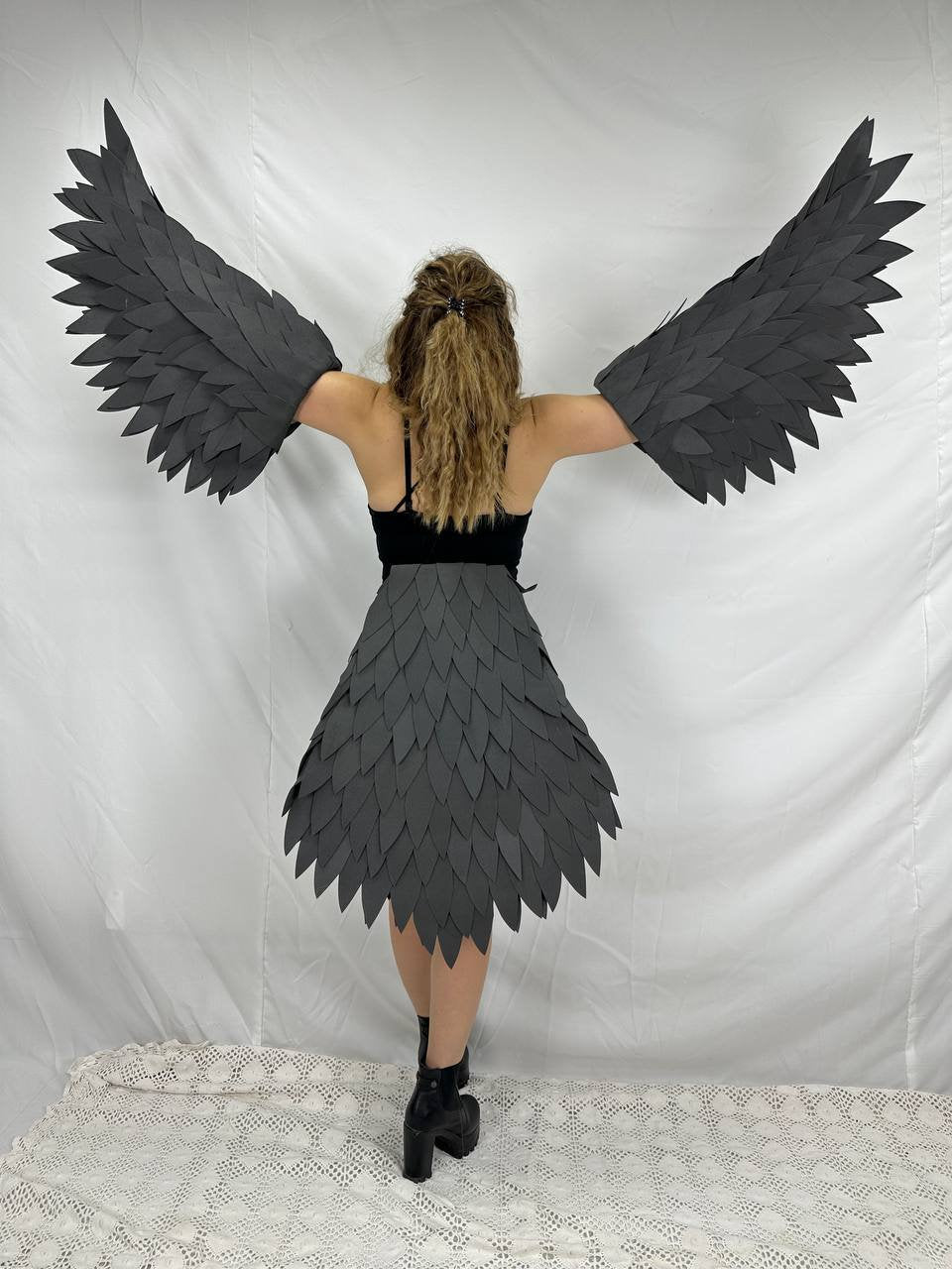 May include: A person wearing a black dress with a gray feather skirt and matching feather wings.