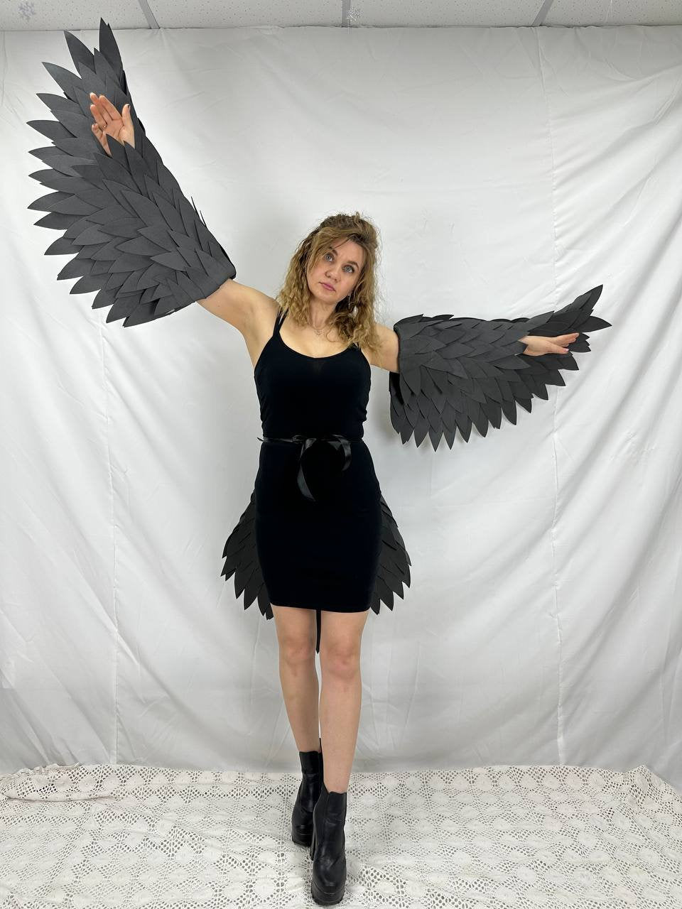 May include: A person wearing a black dress with black feathered wings attached to their arms. The wings are made of paper or cardboard and are shaped like bird wings.