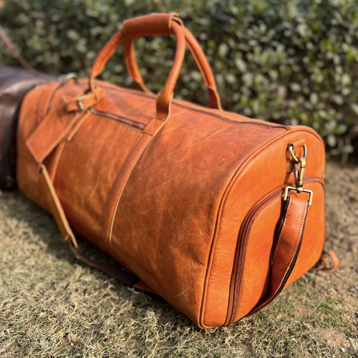 May include: A large, orange leather duffel bag with a top handle and a shoulder strap. The bag has a zippered closure and a small pocket on the front.