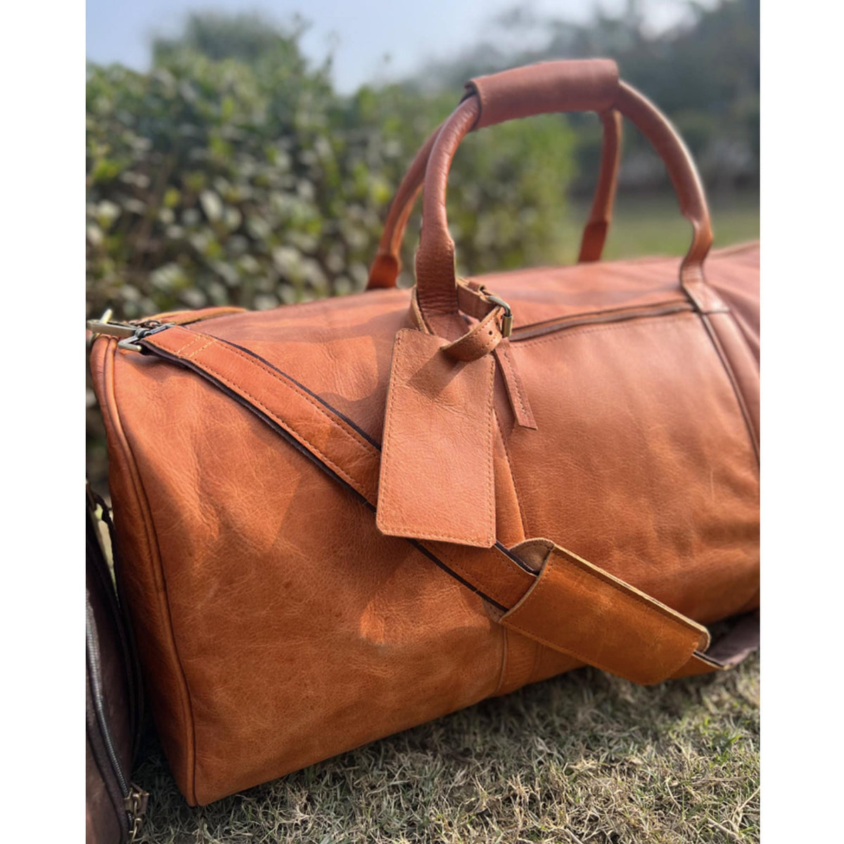 May include: A brown leather duffel bag with a top handle and a detachable shoulder strap. The bag has a leather tag attached to it.