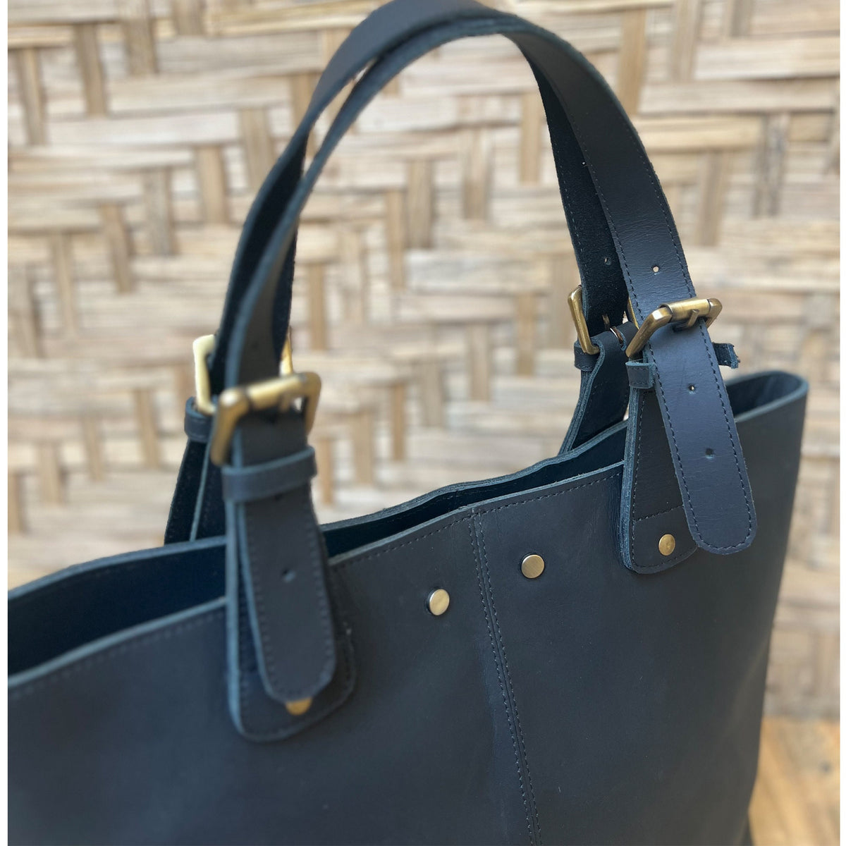 May include: A dark blue leather tote bag with two adjustable straps and brass buckles. The bag has a top zipper closure and a spacious interior.
