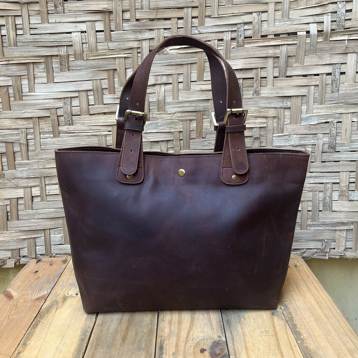 May include: A brown leather tote bag with two adjustable straps and brass buckles. The bag has a simple design and is made of high-quality leather.