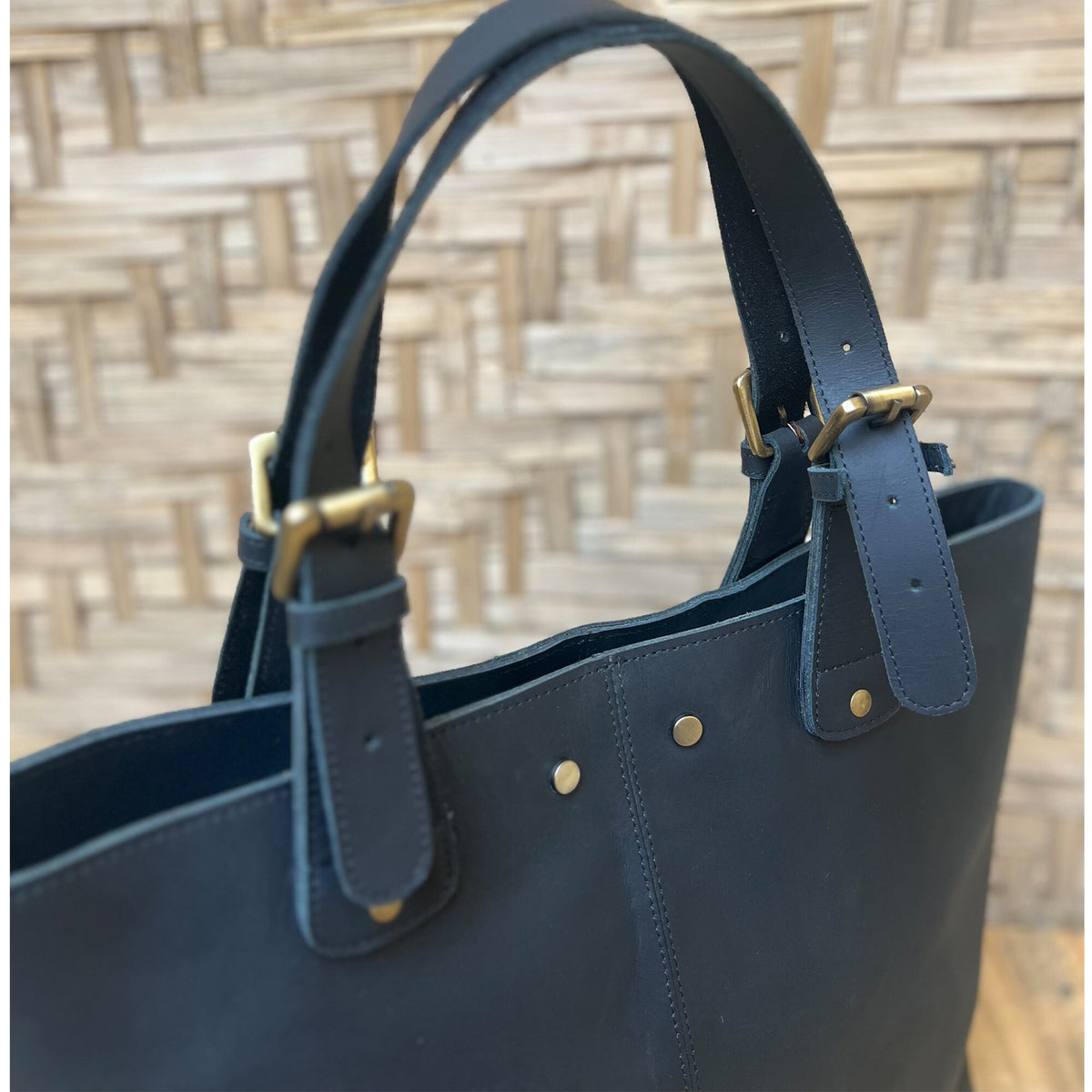 May include: A dark blue leather tote bag with two adjustable straps and brass buckles. The bag has a top zipper closure and a spacious interior.