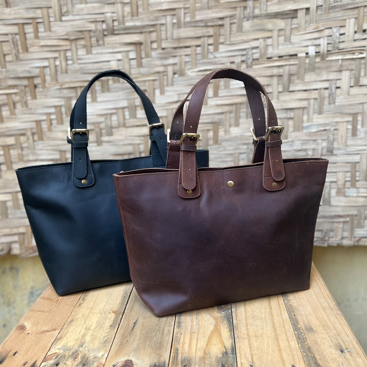 May include: Two leather tote bags, one black and one brown, with double buckle straps and a gold button closure.