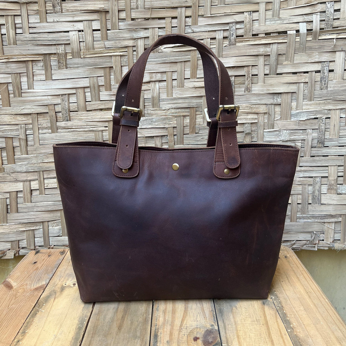 May include: A brown leather tote bag with two adjustable straps and gold buckles. The bag has a simple design and is made of high-quality leather.