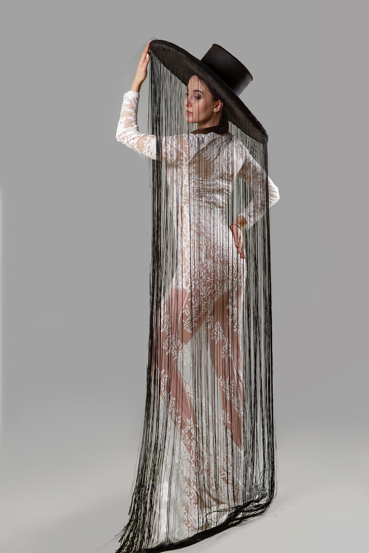 May include: A woman wearing a white lace dress with a black wide-brimmed hat with long fringe hanging down the back.