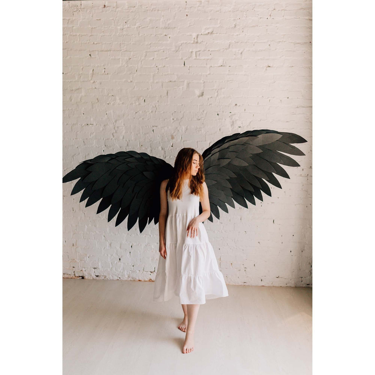 May include: A person wearing a white dress with large black angel wings. The wings are made of feathers and are spread out behind the person.