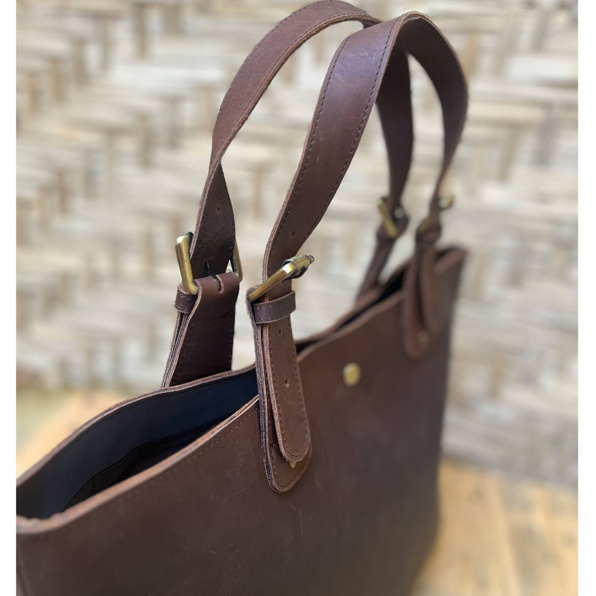May include: A brown leather tote bag with two adjustable straps and brass buckles. The bag has a dark blue lining.