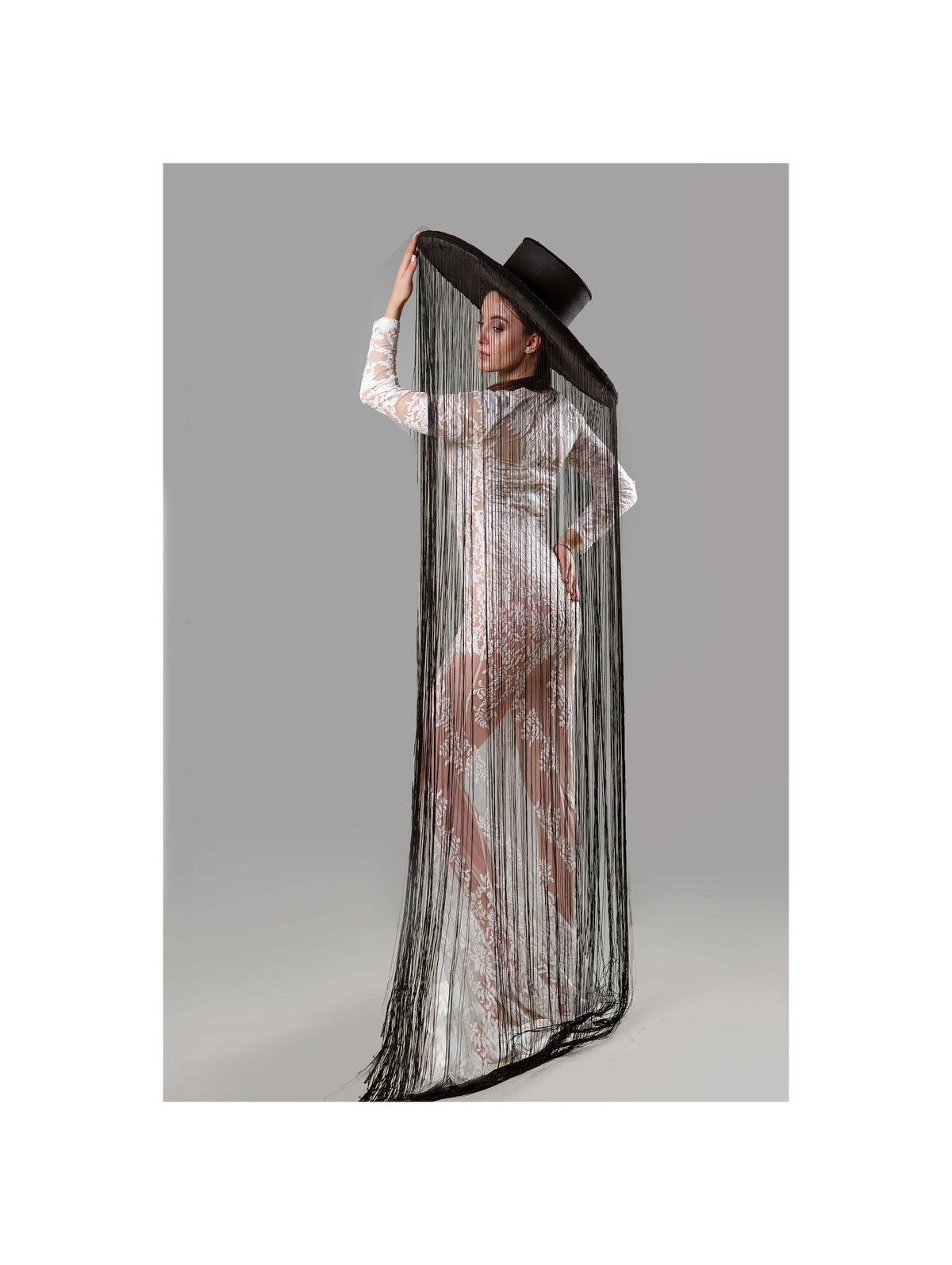 May include: A woman wearing a white lace dress with a black wide-brimmed hat with long black fringe hanging down the back.