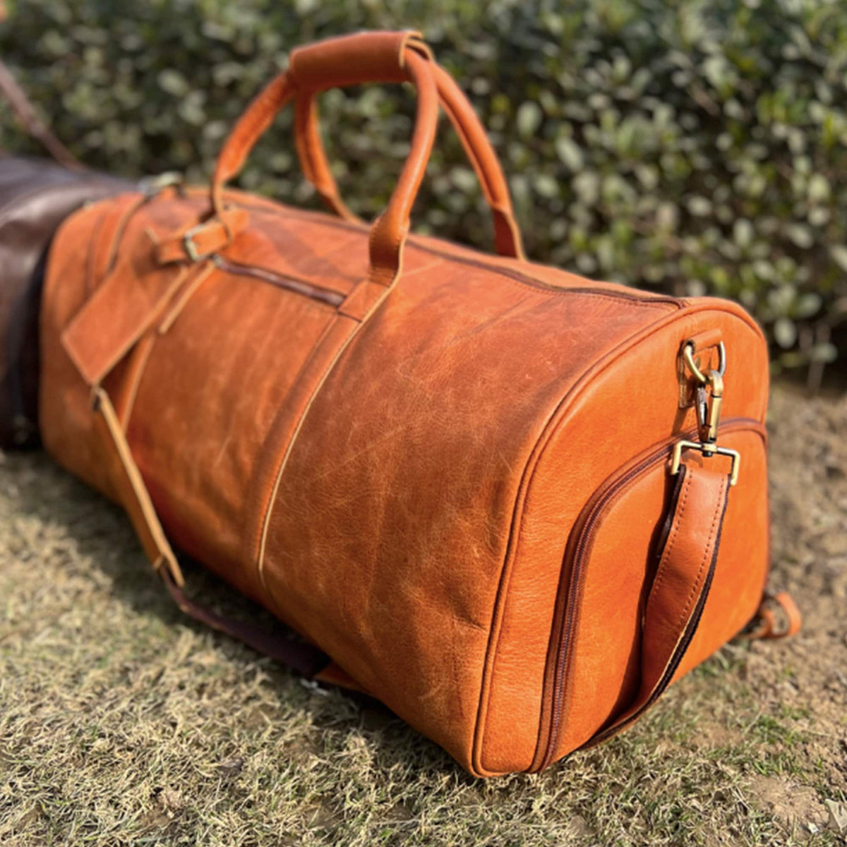 May include: A large, orange leather duffel bag with a top handle and a shoulder strap. The bag has a zippered closure and a small pocket on the front.