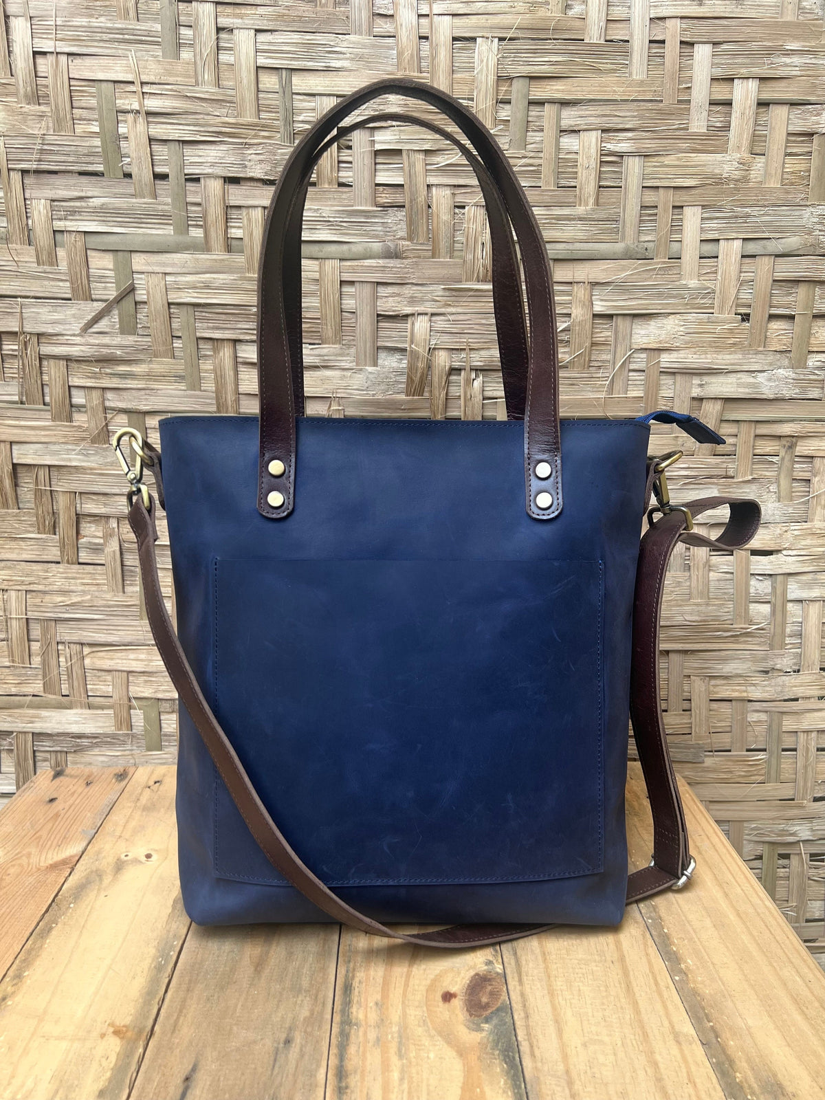 May include: A dark blue leather tote bag with brown leather straps and a front pocket. The bag has a zipper closure and a detachable shoulder strap.