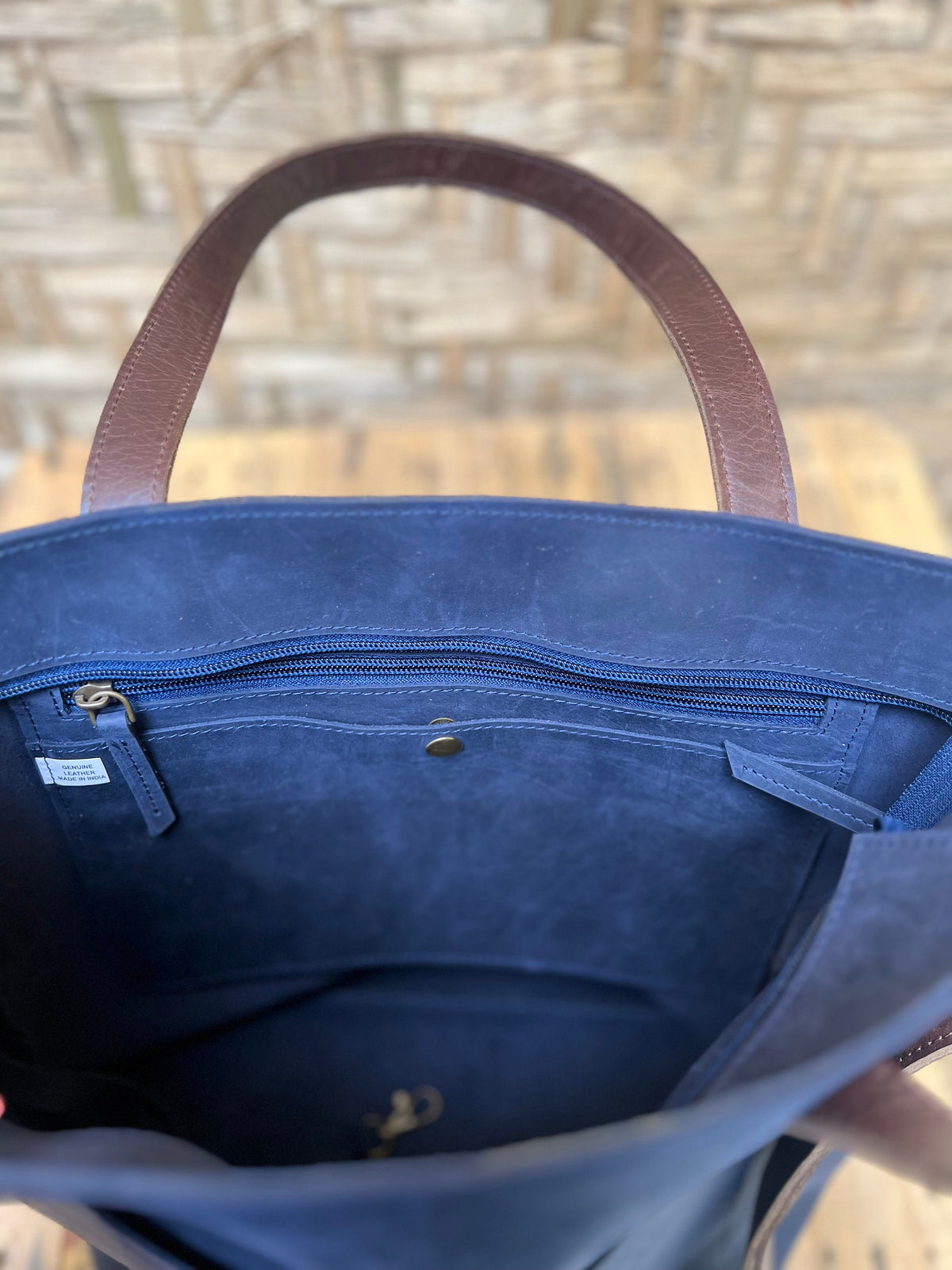 May include: The inside of a navy blue leather tote bag with a brown leather handle. The bag has a zippered pocket and a small leather tag that says "Genuine Leather".