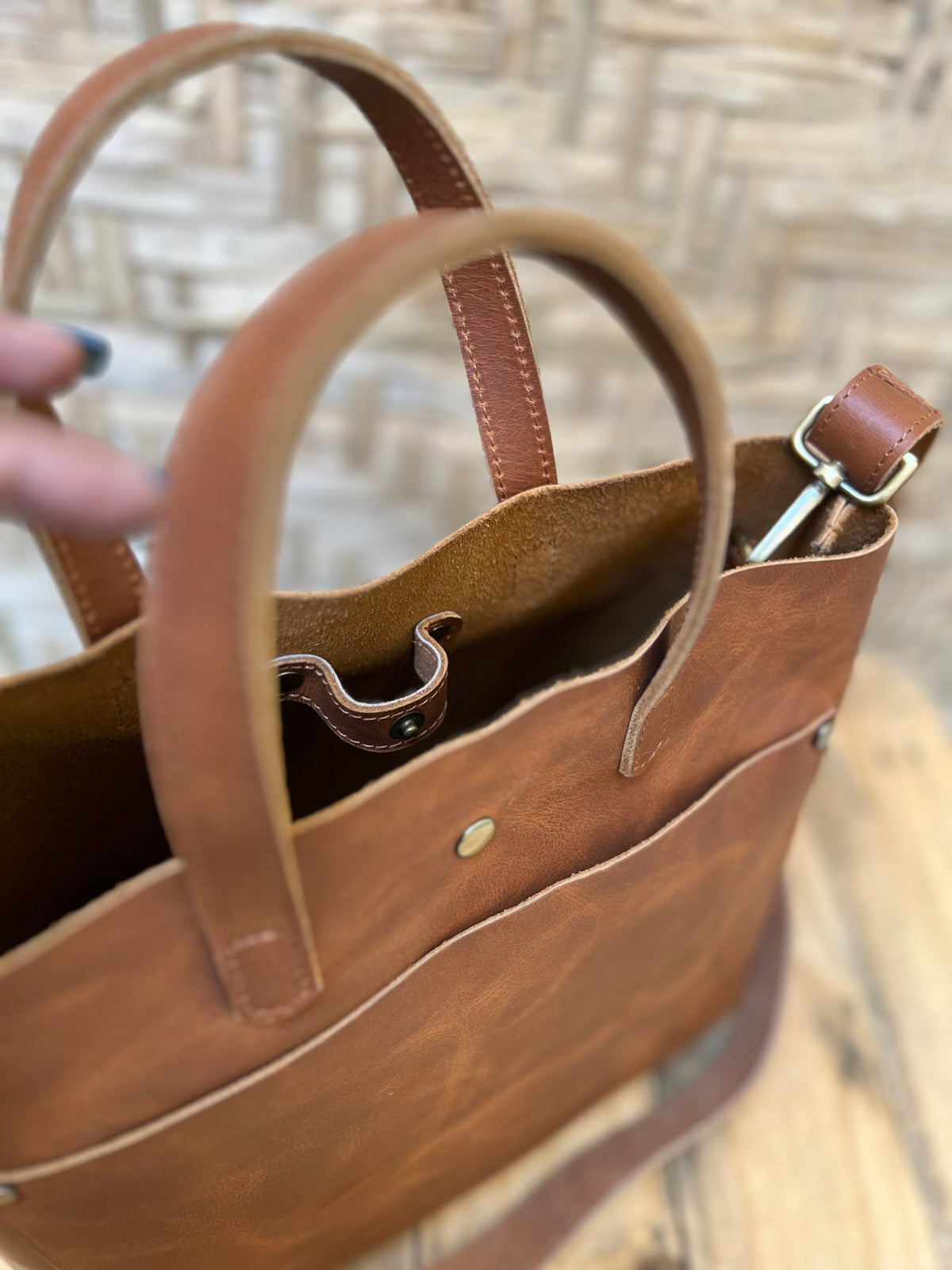 May include: A brown leather tote bag with a single pocket on the front. The bag has two top handles and a long strap.