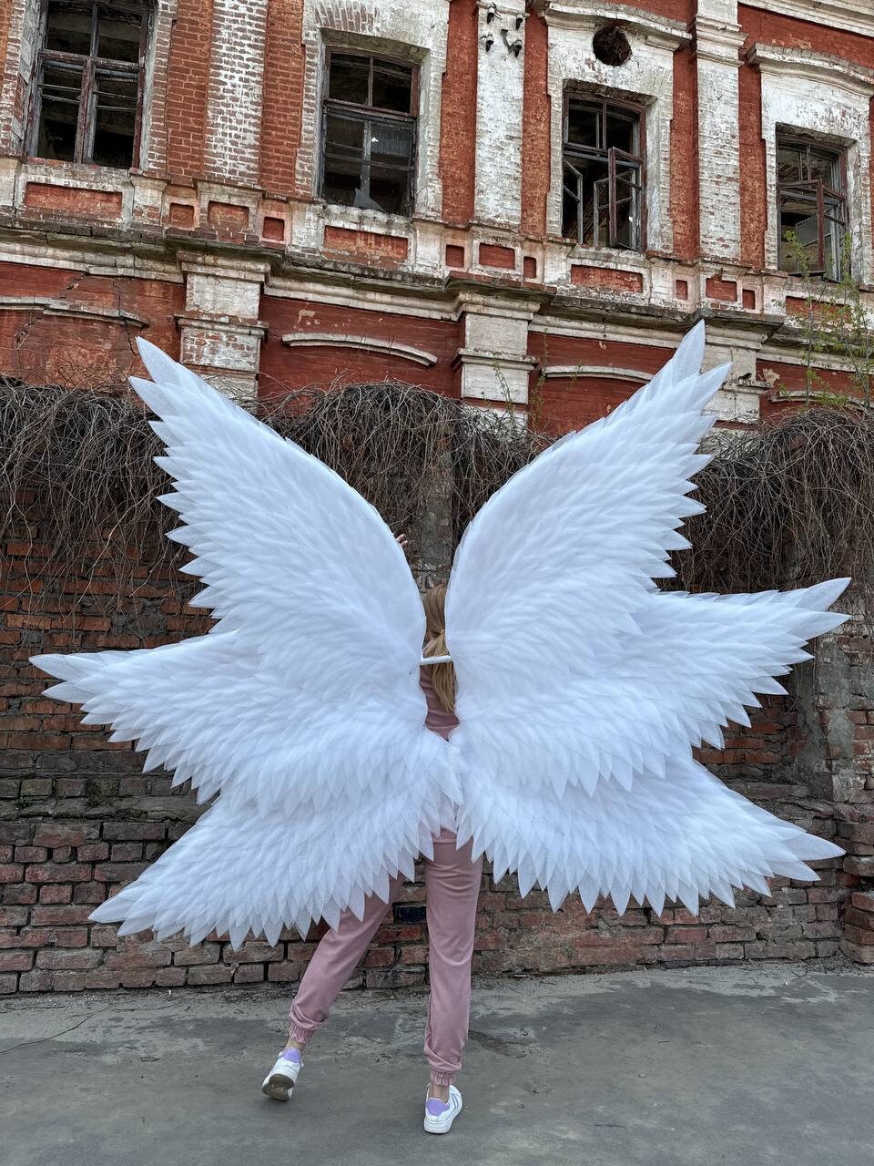 May include: A person wearing a pink outfit with large white angel wings. The wings are made of feathers and are very detailed.