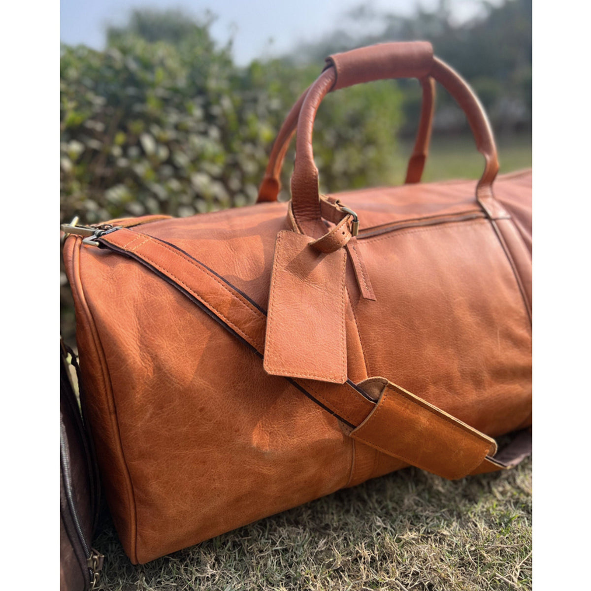May include: A brown leather duffel bag with a top handle and a detachable shoulder strap. The bag has a leather tag attached to it.