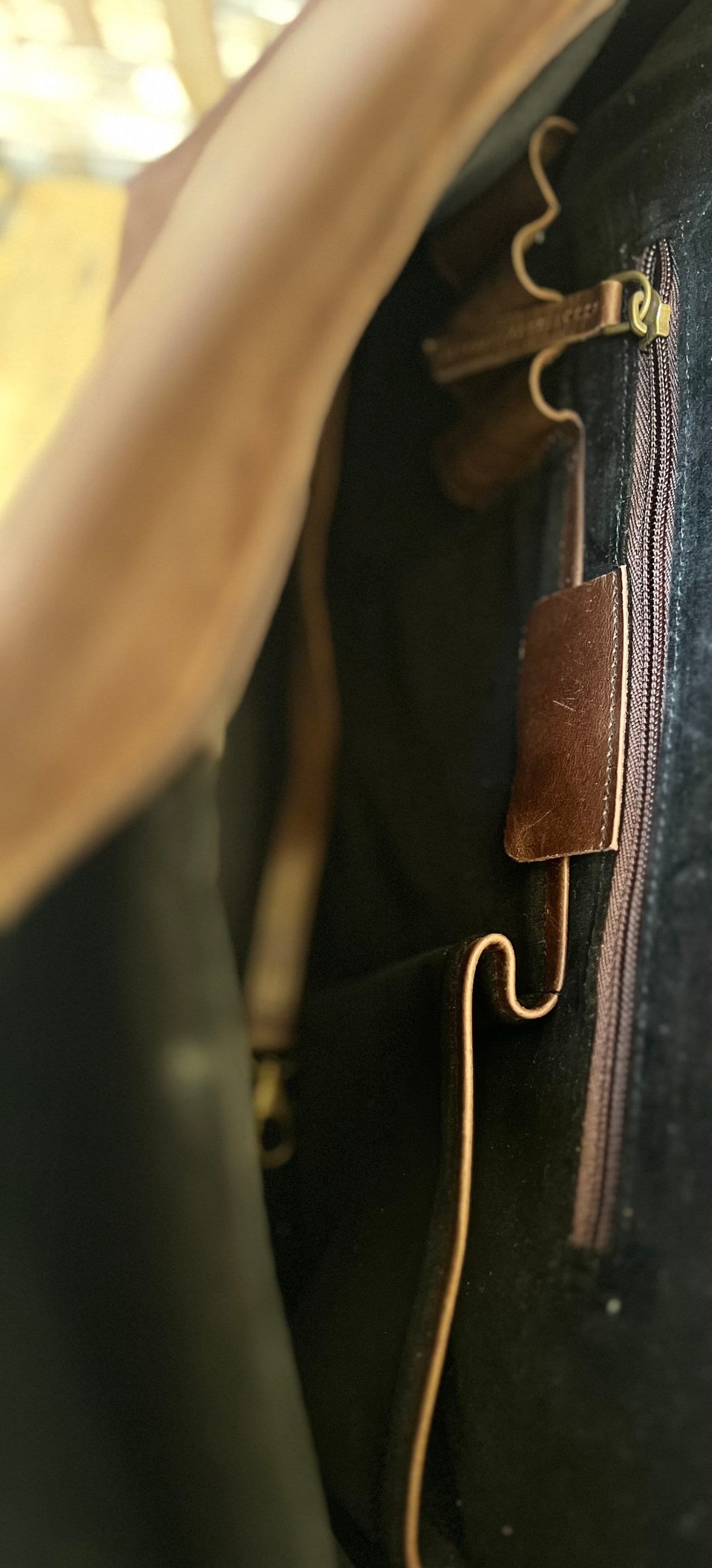 May include: Close-up of a dark brown leather bag interior with a zipper and a leather tab. The bag has a black interior and a light brown strap. The zipper pull is gold.