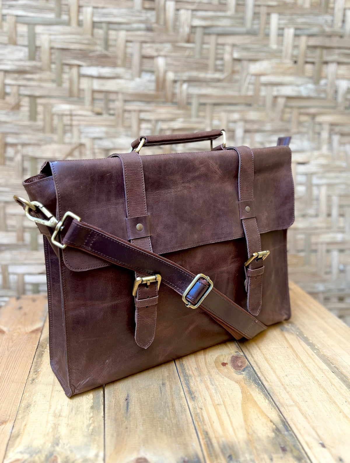 May include: A brown leather briefcase with a shoulder strap and two buckles. The briefcase has a top handle and a flap closure.