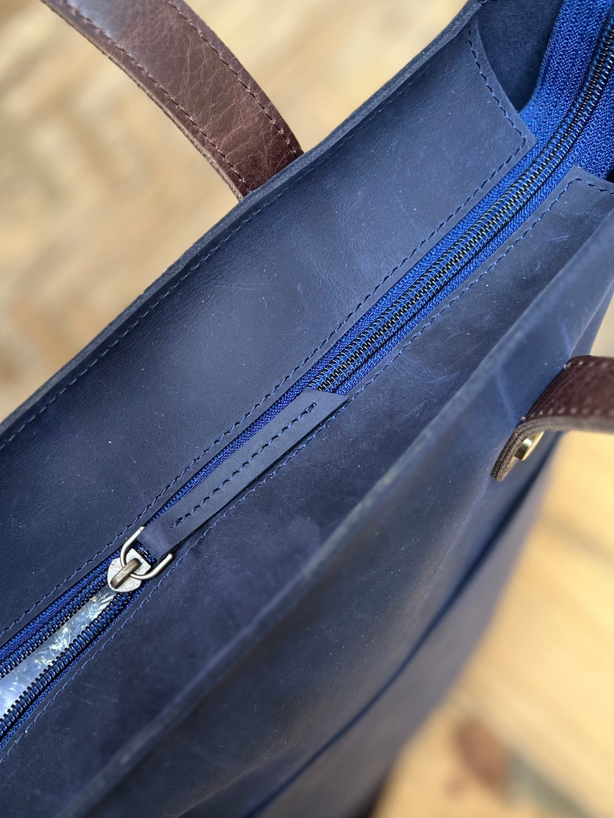 May include: A navy blue leather tote bag with a brown leather handle and a zipper closure.