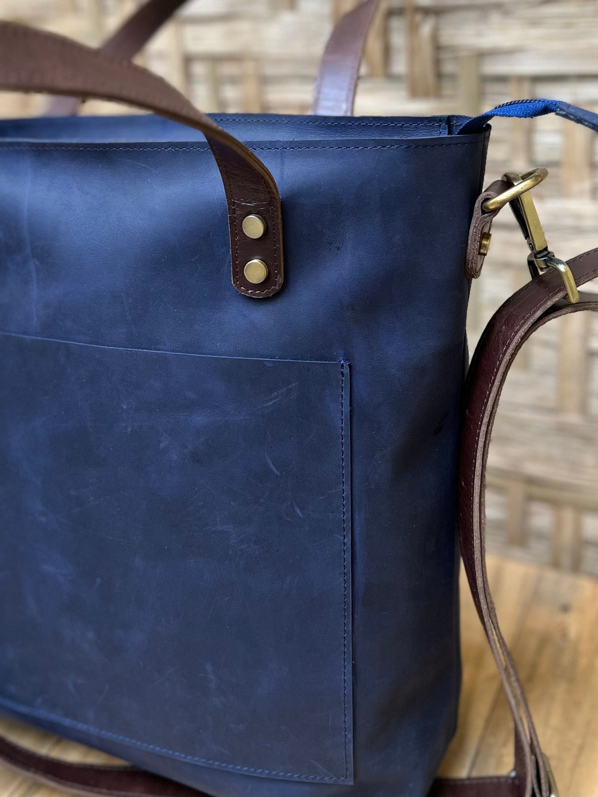 May include: A dark blue leather tote bag with brown leather straps and a pocket on the front. The bag has a brass buckle and a detachable shoulder strap.