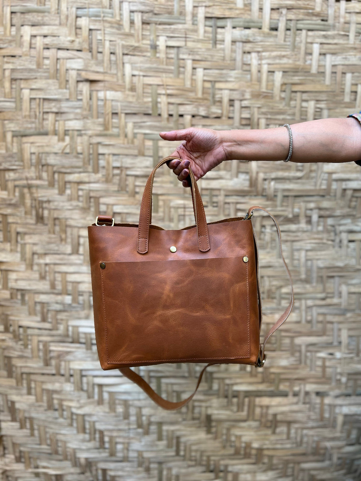 May include: A brown leather tote bag with a front pocket and a long strap. The bag has a worn, distressed look.