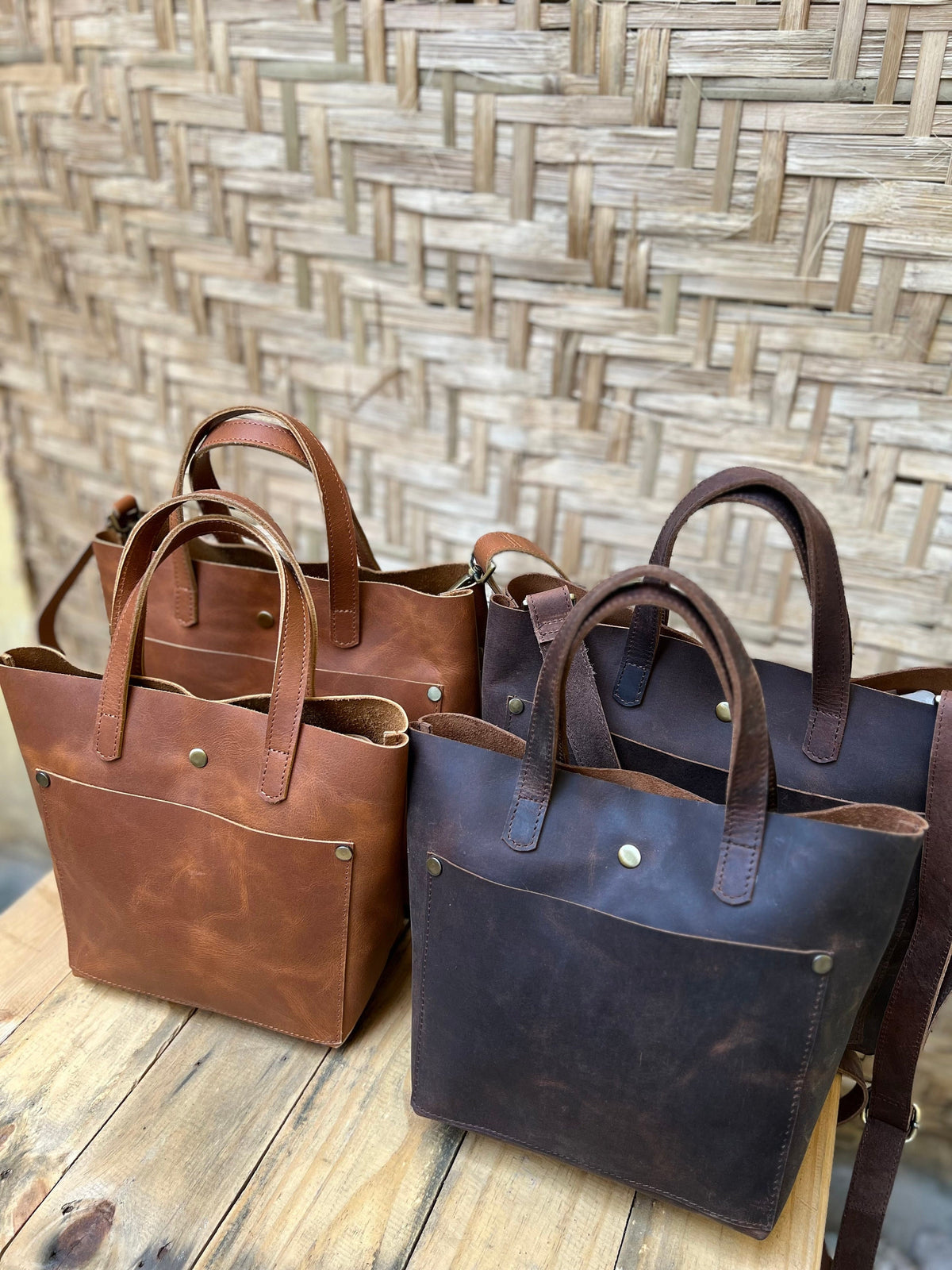 May include: Three leather tote bags in brown and dark brown. The bags have a single pocket on the front and a top handle.