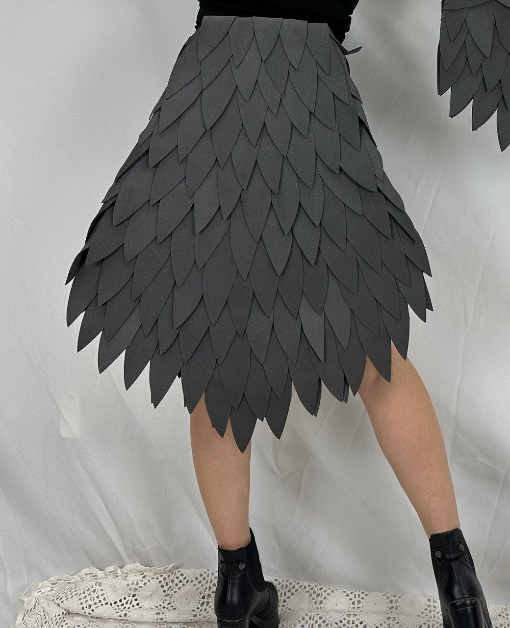 May include: A gray skirt made of fabric that resembles overlapping leaves. The skirt is short and has a high waist.