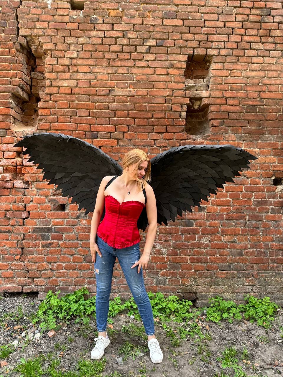 May include: A person wearing a red corset and blue jeans with large black feathered wings.