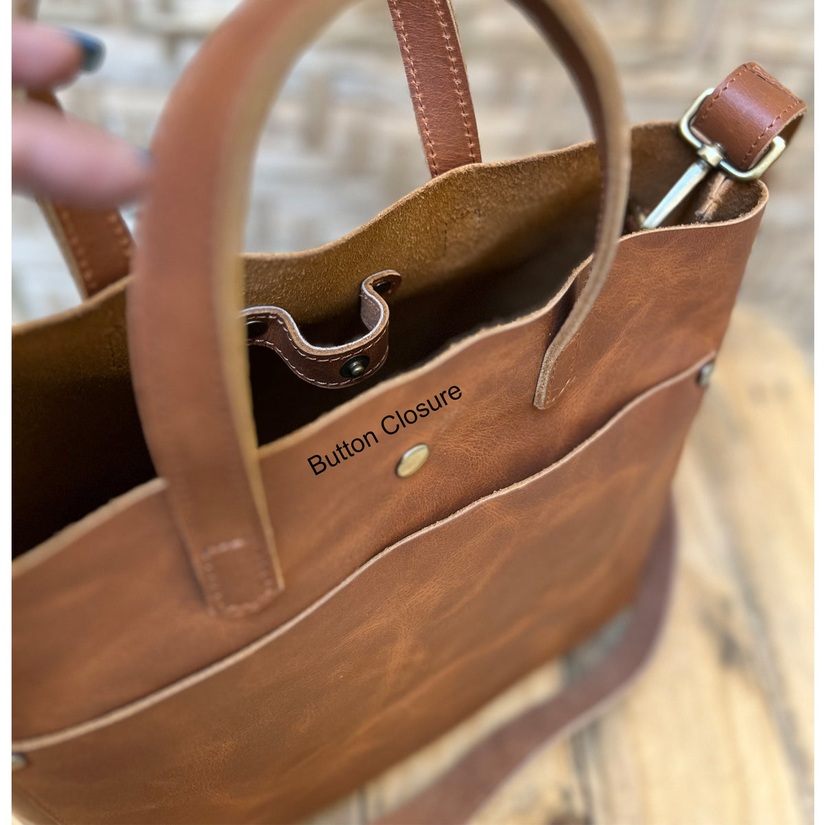 May include: A brown leather tote bag with a button closure. The bag has a large pocket on the front and a long strap.