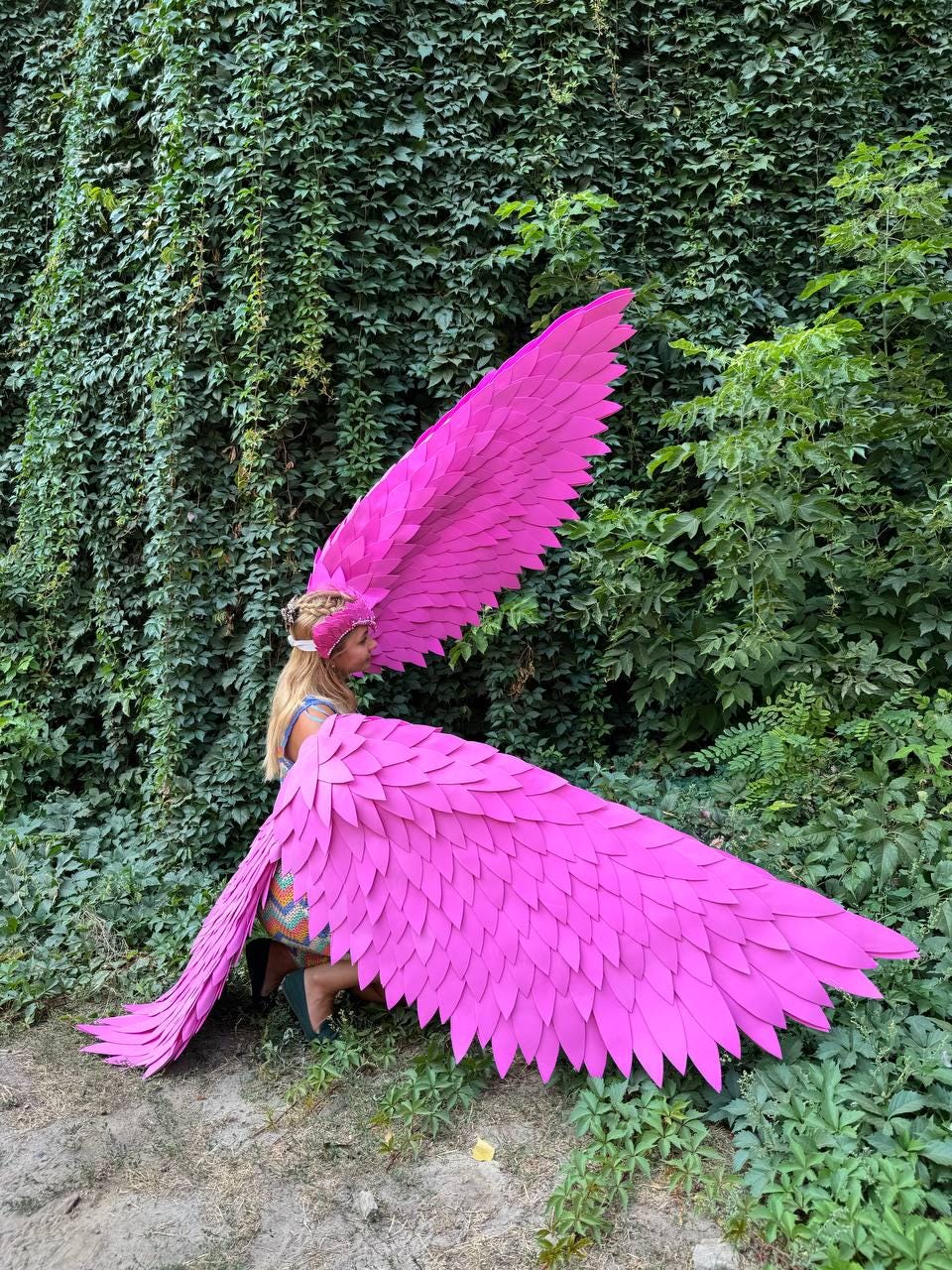 May include: A person wearing a pink feathered angel costume with large wings. The wings are made of many individual feathers and are spread out behind the person.