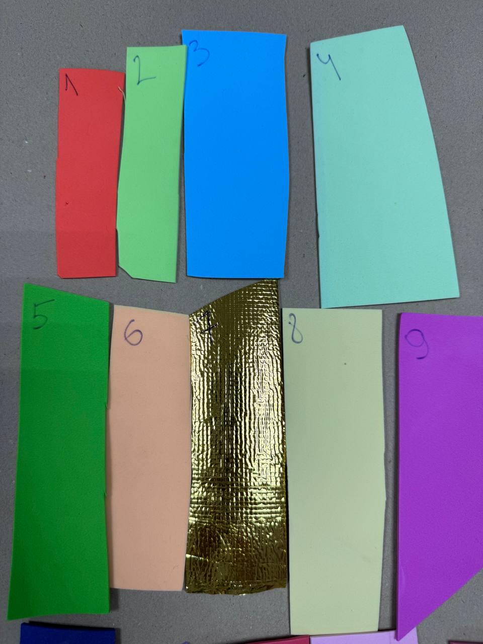May include: Nine different colored swatches of foam material, numbered 1 through 9. The swatches are arranged in two rows, with the top row containing swatches 1 through 4 and the bottom row containing swatches 5 through 9. The swatches are all rectangular in shape and are approximately the same size. The colors of the swatches are red, green, blue, light green, dark green, peach, gold, light yellow, and purple.