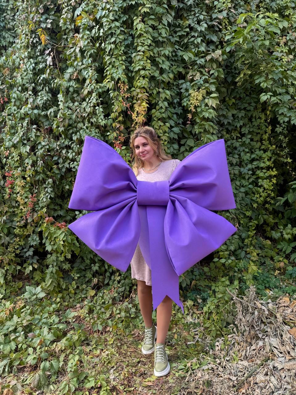 May include: A large purple bow with a long tail. The bow is made of fabric and is tied around the waist of a person.