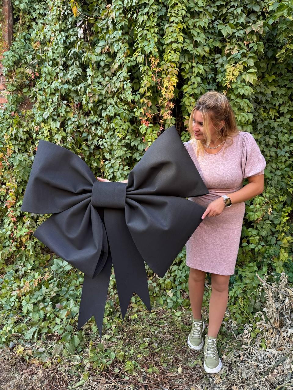 May include: A large black fabric bow with long tails. The bow is large enough to be held by a person standing in front of it.