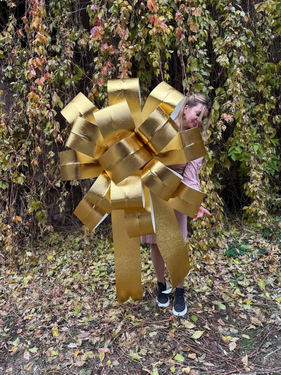 May include: A large gold bow made of multiple layers of ribbon. The bow is standing upright and is taller than a person.
