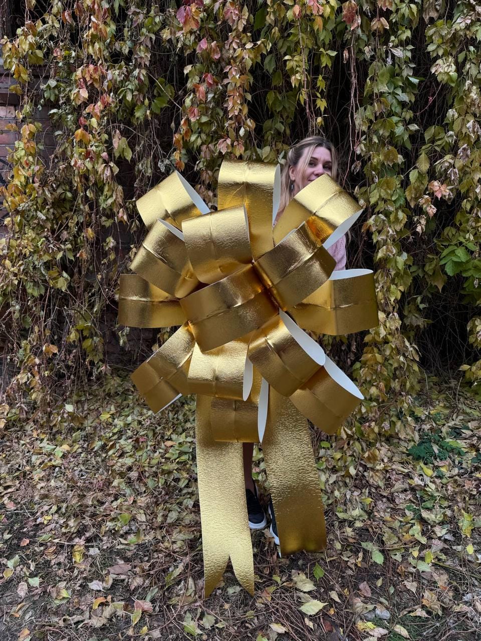 May include: A large, gold, metallic bow with long streamers. The bow is made of multiple layers of shiny, textured material.