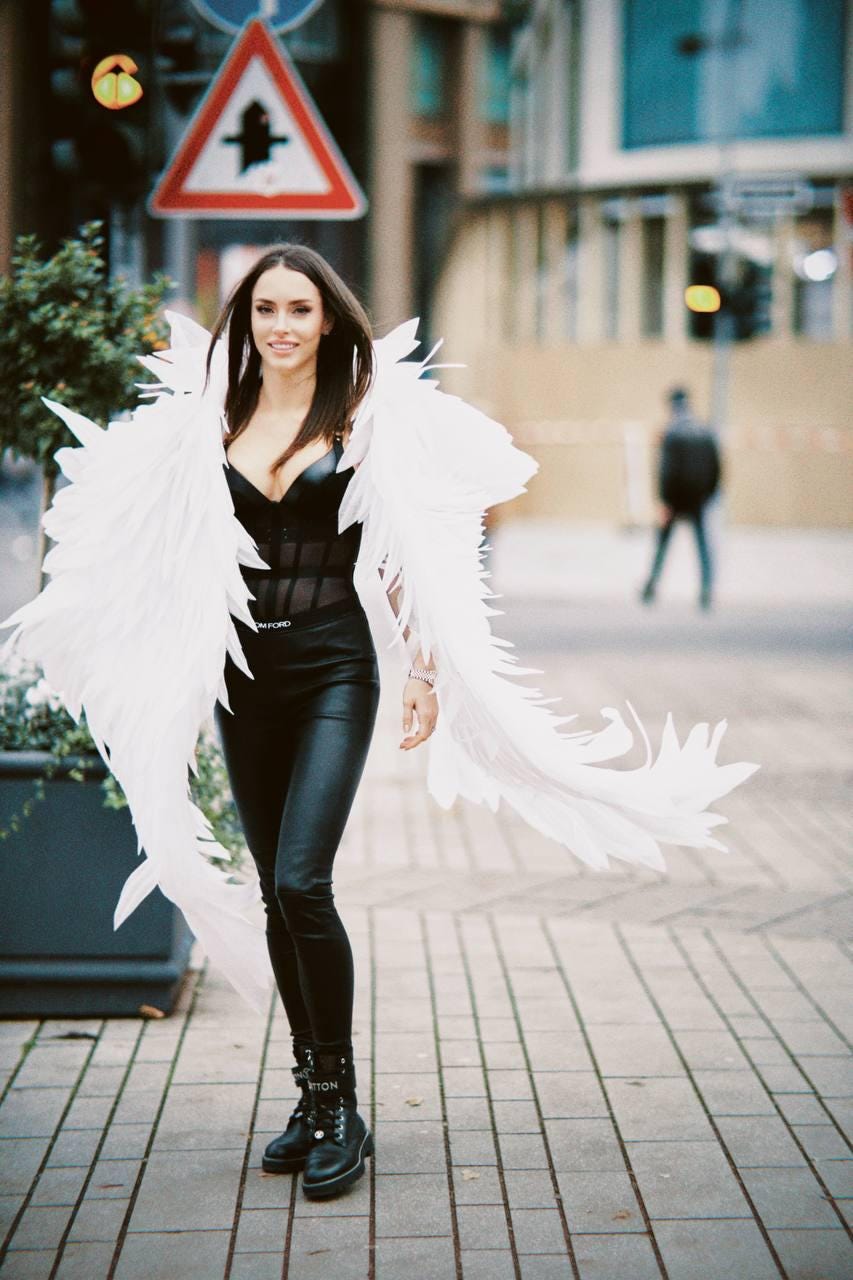 May include: A woman wearing a black corset top, black leather pants, and black boots with white angel wings.
