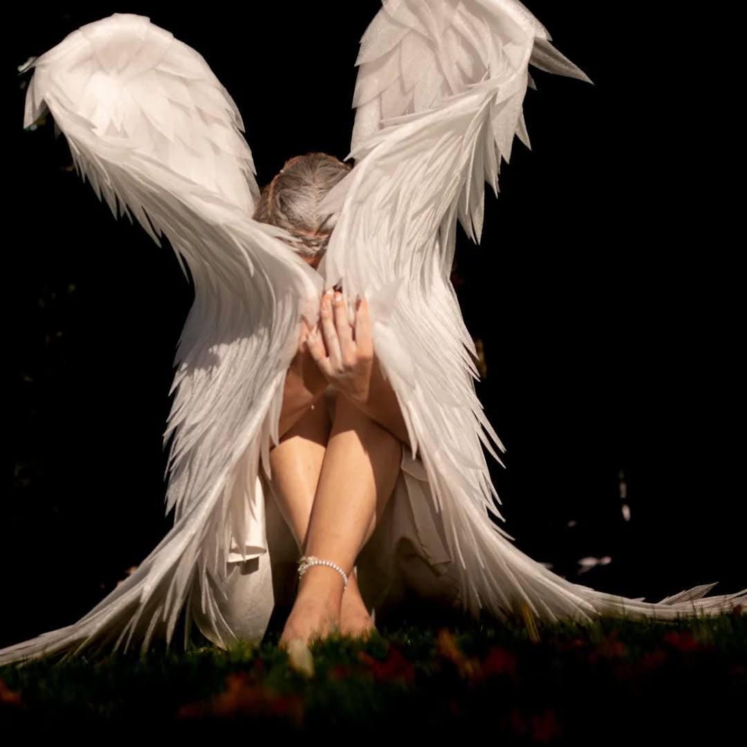 May include: A person wearing a white costume with large, feathery wings, sitting on the ground with their head down. The wings are covering the person's face.
