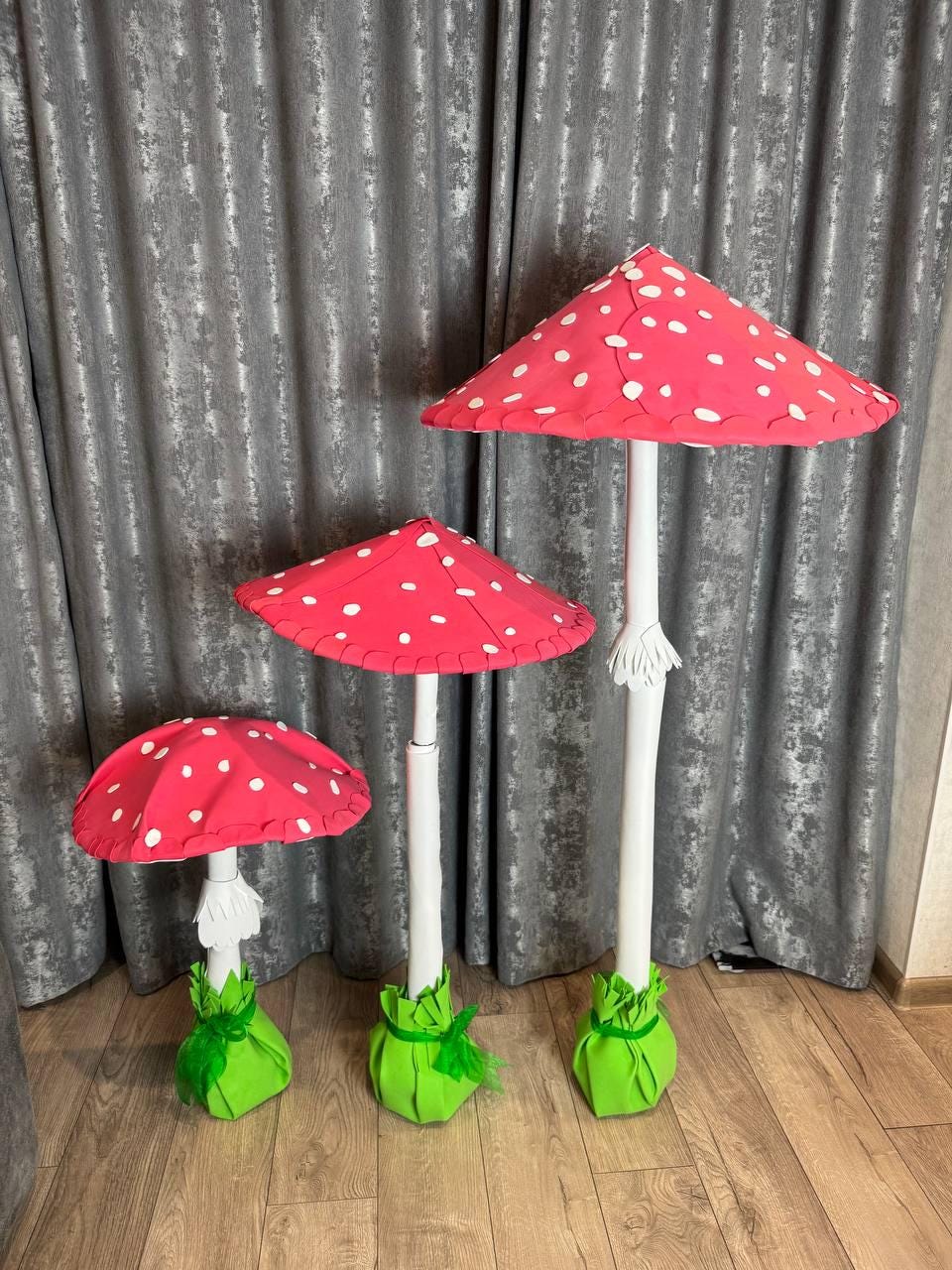 May include: Three red and white mushroom-shaped decorations with green bases. The mushrooms are made of paper and have white polka dots. The largest mushroom is about 30 inches tall.