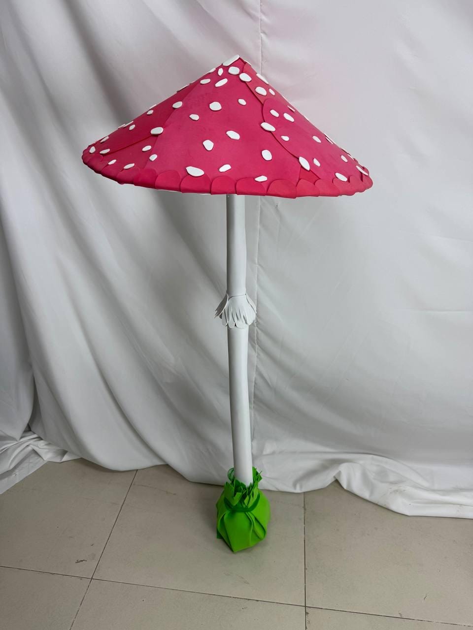 May include: A large, pink and white mushroom made of paper. The mushroom has a white stem and a green base.
