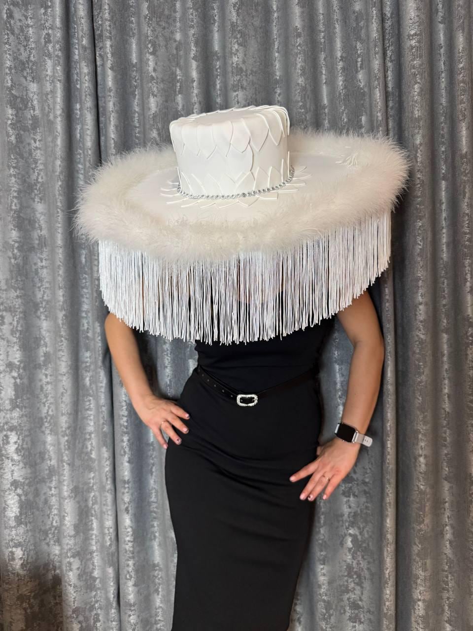 May include: A white hat with a wide brim and a feathered trim. The hat is decorated with white feathers and a white ribbon.