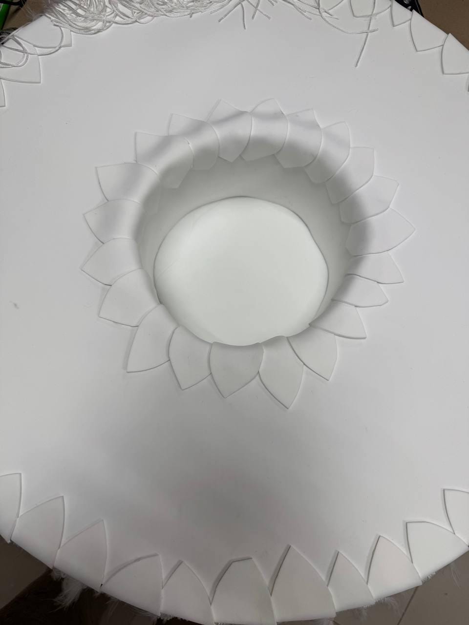 May include: White circular base with a scalloped edge and a smaller circular opening in the center. The opening is surrounded by a ring of white petals.