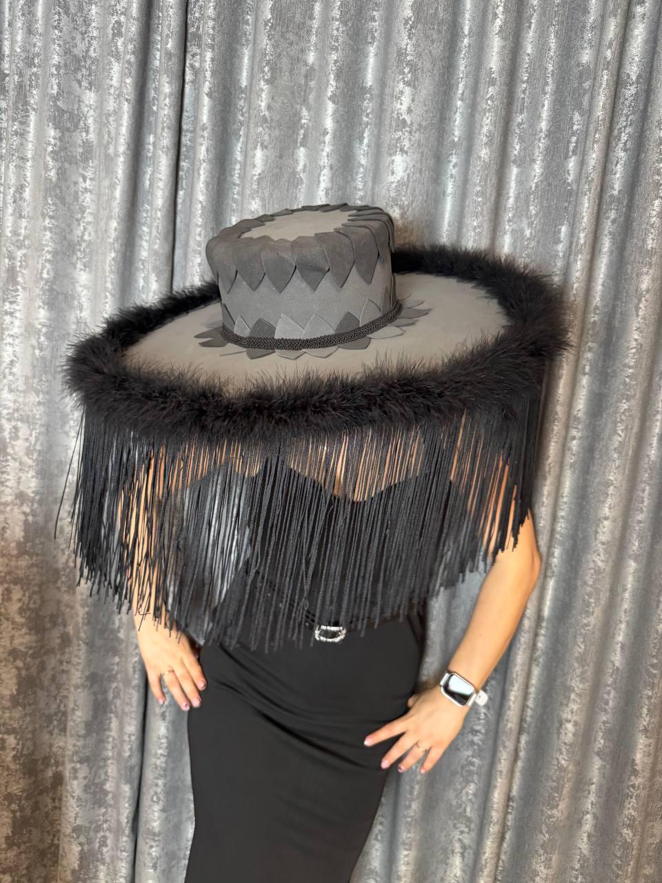 May include: A gray hat with a wide brim, adorned with black fringe and feathers. The hat features a decorative crown and a dark trim. The hat is a unique fashion accessory.