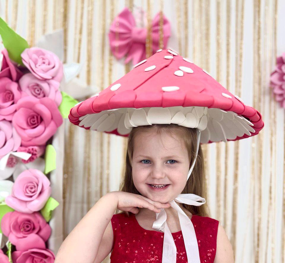 May include: A whimsical mushroom hat with a red cap and white spots. The hat has a white underside and is worn with a white ribbon. The hat is part of a costume or accessory, perfect for themed events or imaginative play.