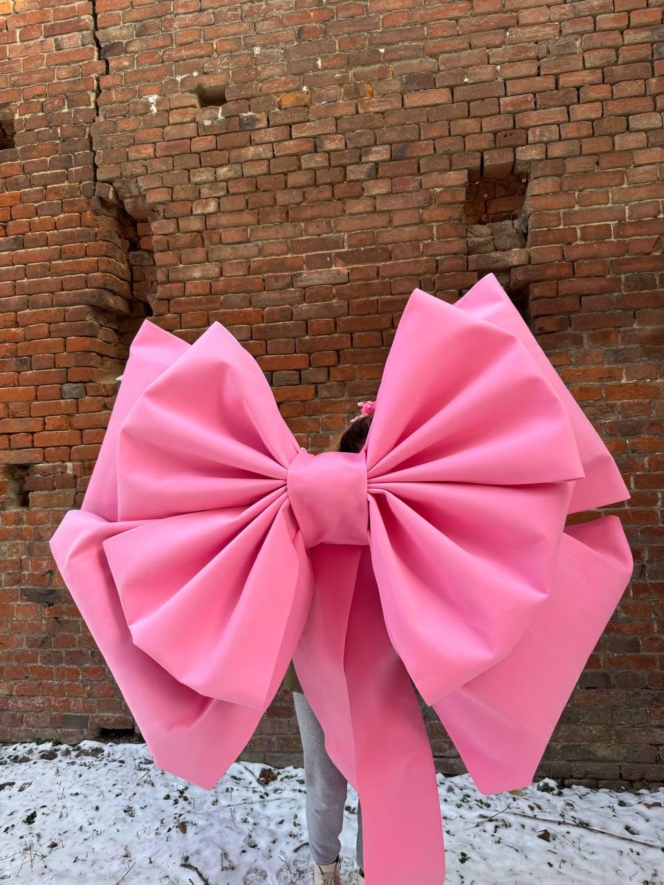 May include: A large pink bow made of fabric. The bow is tied around a person's waist and the ends of the bow are trailing behind them.
