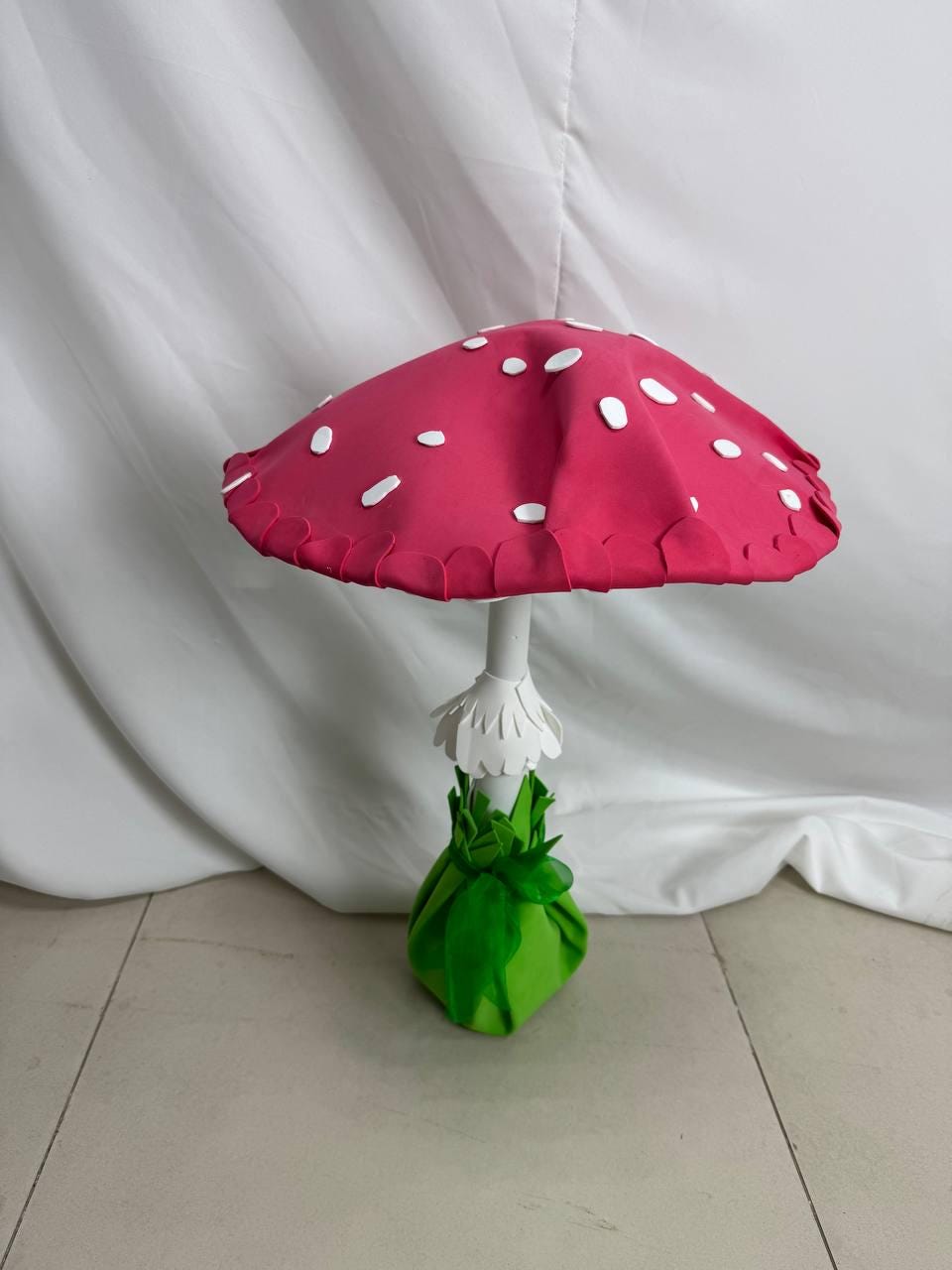 May include: A large, pink and white mushroom made of felt. The mushroom has a scalloped edge and white dots on the top. The stem is white and the base is green.