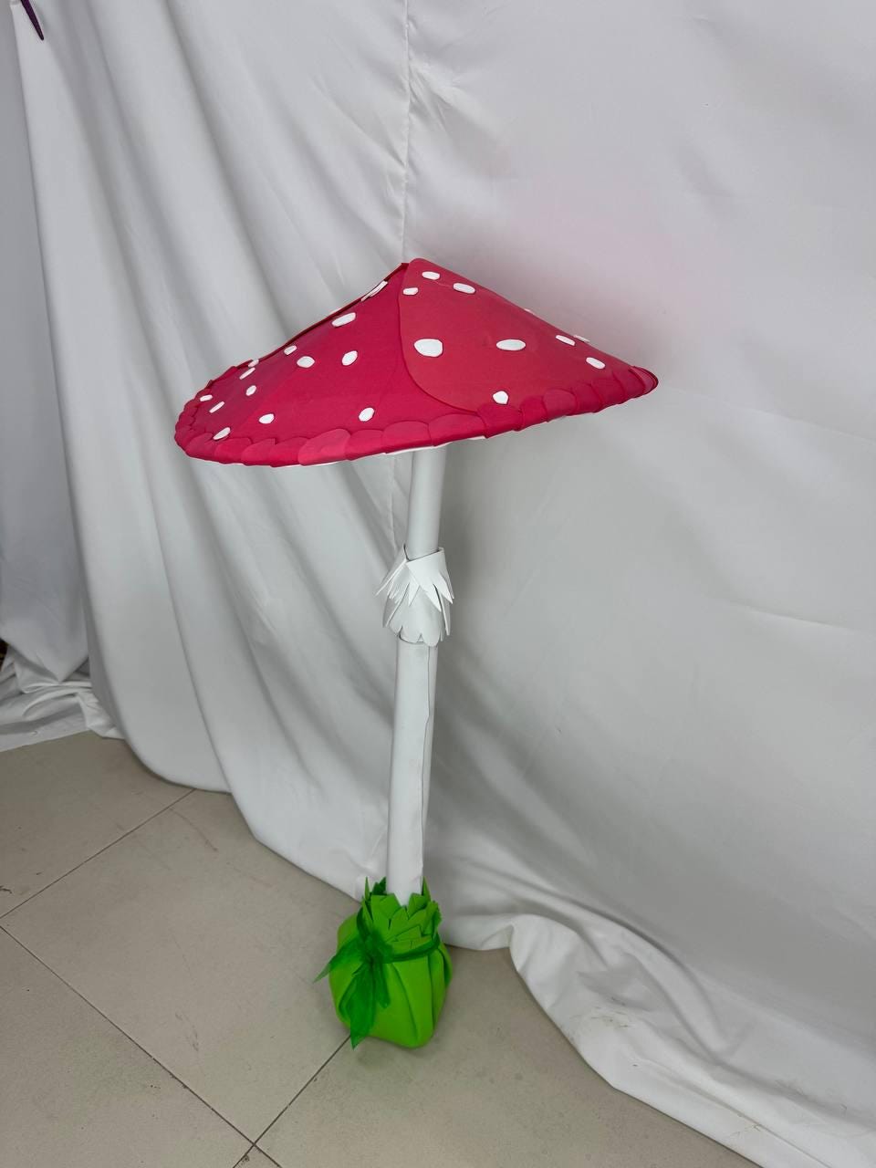 May include: A large, red and white paper mushroom with white polka dots. The mushroom has a white stem and a green base.