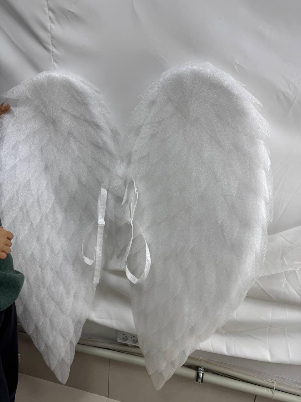 May include: A pair of white angel wings with a feathery texture. The wings are attached to each other with white straps.