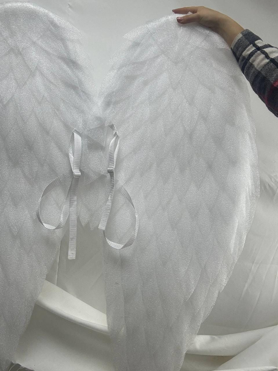 May include: White angel wings with a textured, feathery design. The wings are attached with white ribbon ties.