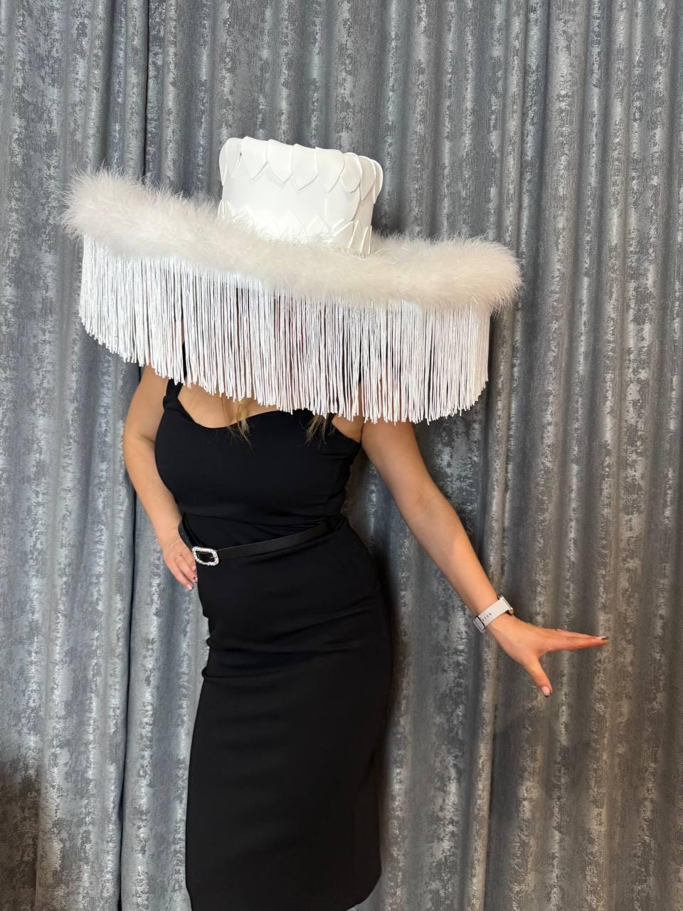 May include: A large white hat with a wide brim and a feathered trim. The hat is decorated with white fringe and has a heart-shaped design on the crown.