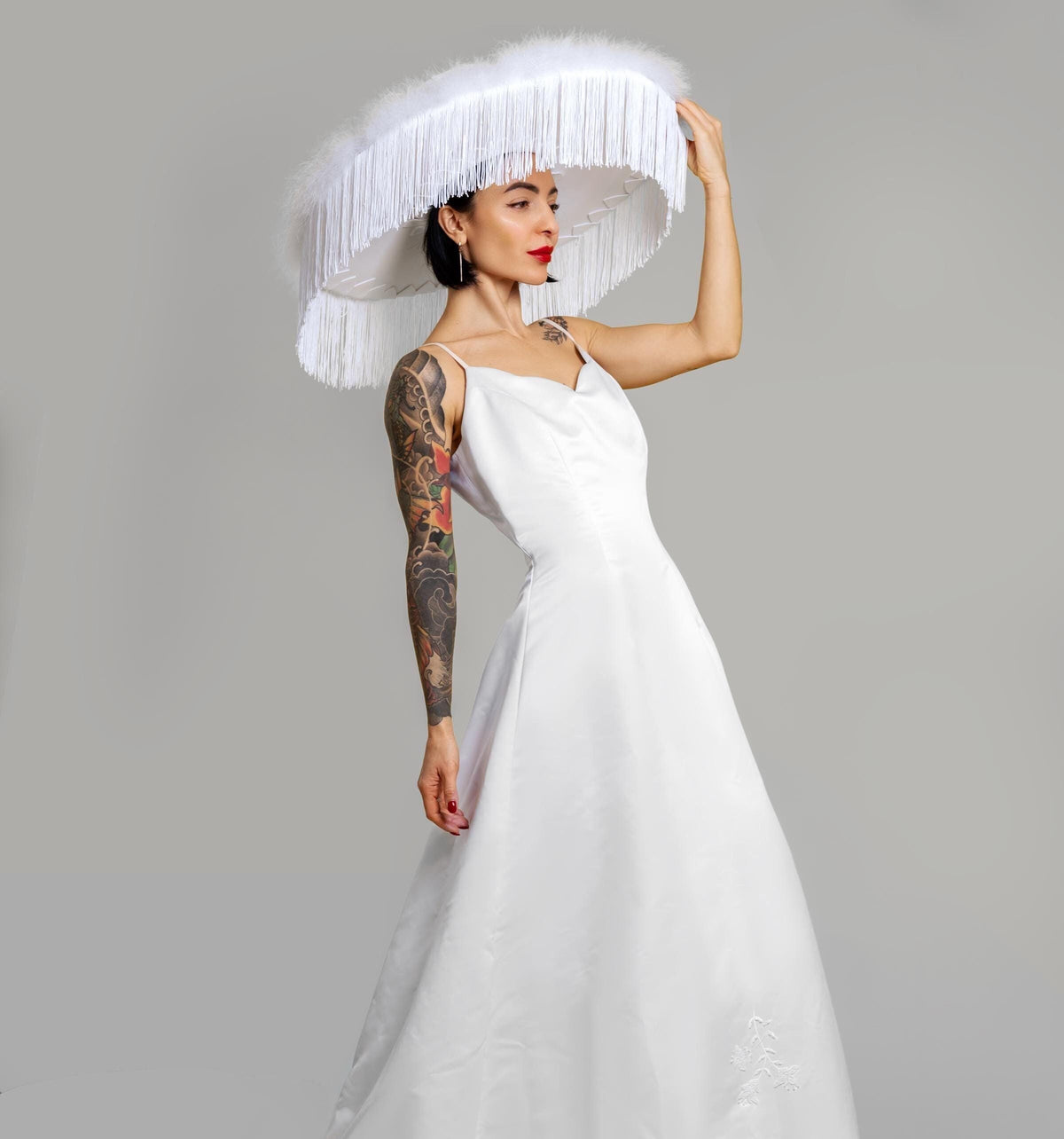 May include: A woman wearing a white dress and a large white hat with a fringe. The hat is decorated with feathers.