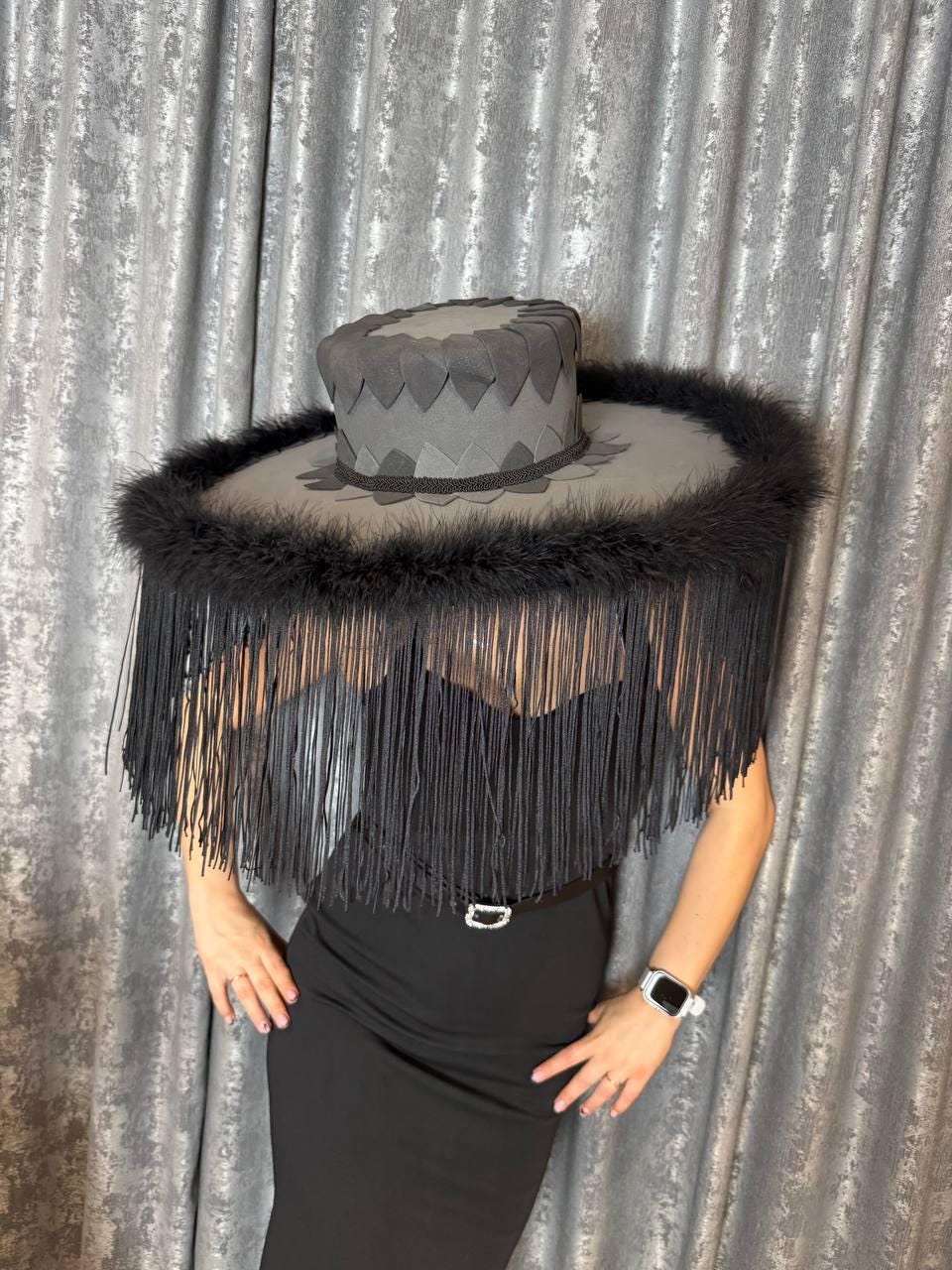 May include: A dramatic, wide-brimmed hat with a gray crown and a circular brim trimmed with black feathers. The brim is adorned with long, black fringe, creating a striking visual effect. The hat is a unique fashion accessory.